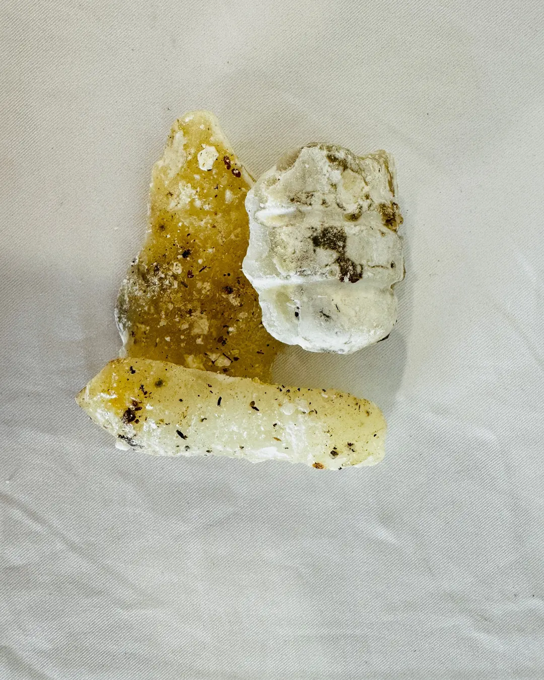 Tres trozos de copal, entre blanco y amarillo translúcido, sobre una tela clara.