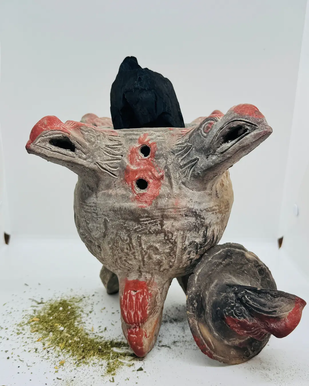 Copalera de barro rojo y gris con forma de animal, con un carbón dentro y la tapa a un lado.
